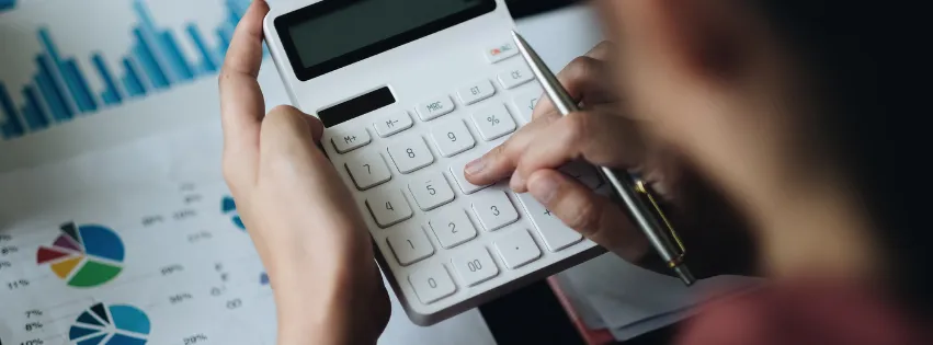 Hands using a calculator over printed financial charts