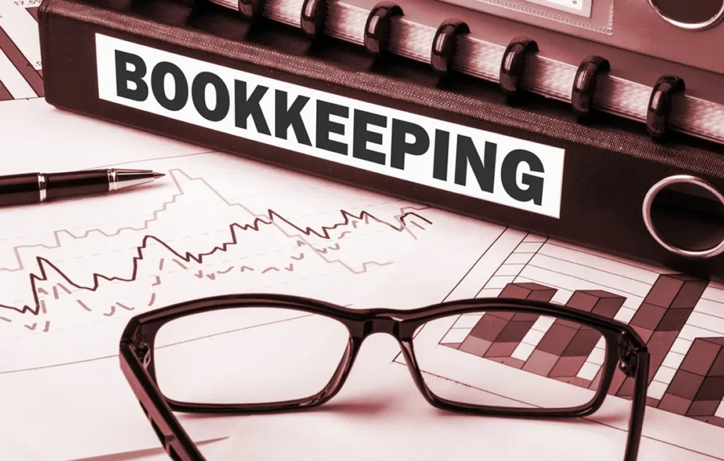 Binder labeled Bookkeeping with eyeglasses resting on a financial chart