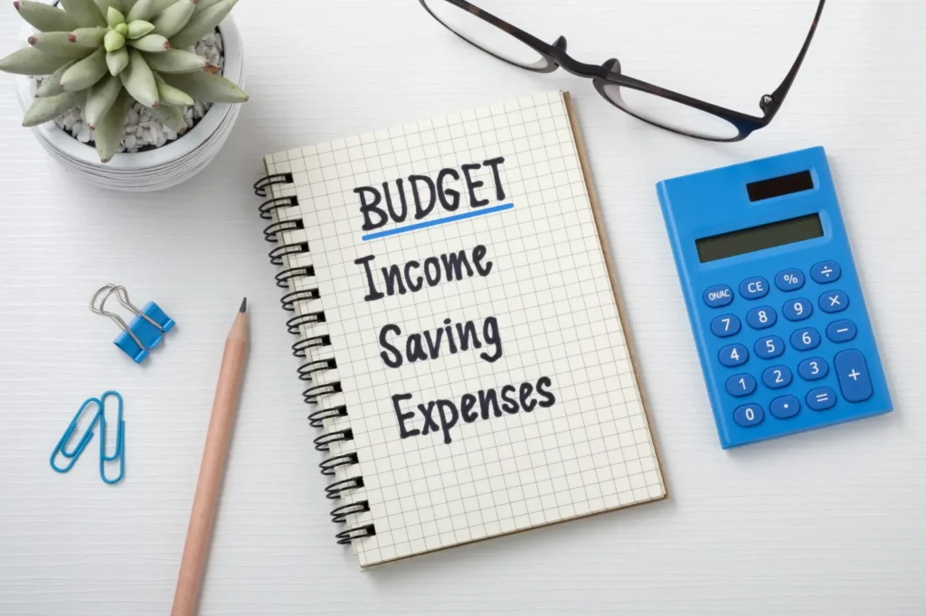 Notebook with a budget of income, saving and expenses next to a calculator and pen