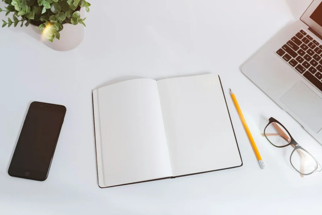 Tidy white desk with an open notebook, phone and laptop