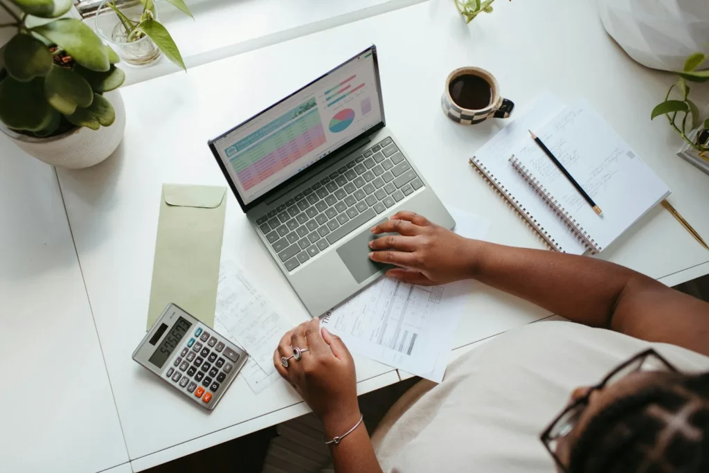 Person working at a laptop beside a calculator and notes