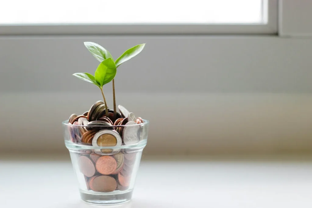 Green seedling growing from a glass of coins