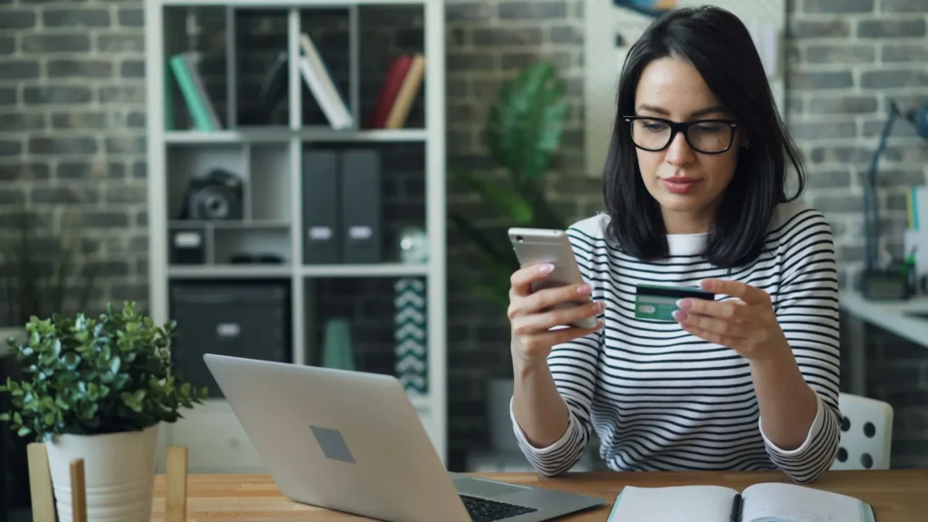 Woman checking her phone while holding a credit card