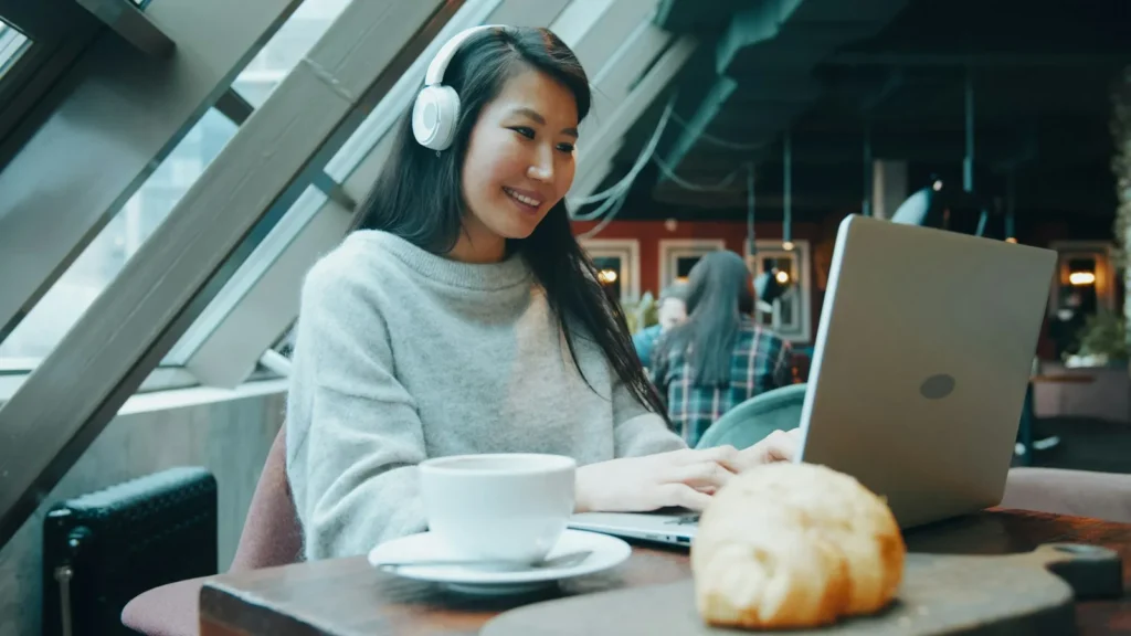 Woman with headphones working on a laptop in a cafe