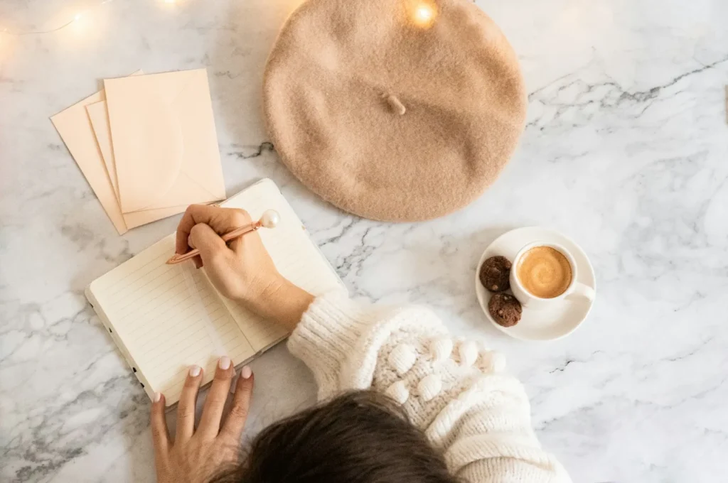 Hand writing in a notebook beside a cup of coffee